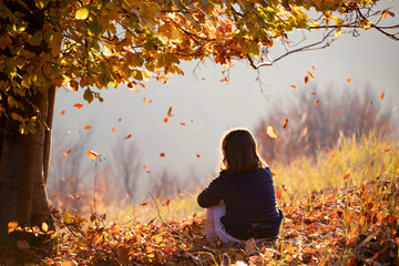 Child sitting in autumn forest in the sunset.