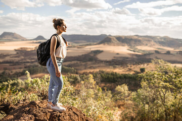 Naklejka na ściany i meble Young Latin girl with backpack enjoying sunset on peak of mountain. Tourist traveler on background valley landscape.