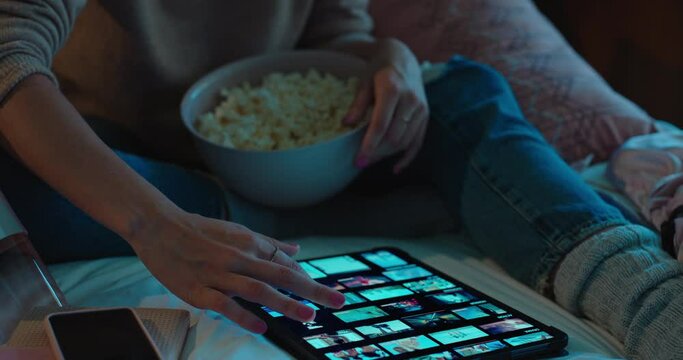 woman using tablet computer browsing online social media at home scrolling through picture gallery looking at creative ideas on screen sitting on bed eating popcorn