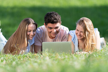 Multiethnic students working together on a laptop laying on the ground. Teamwork in adolescence age concept.