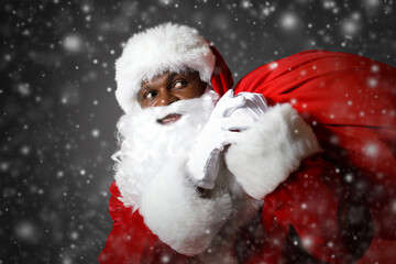 African-American Santa Claus with bag full of gifts on dark background