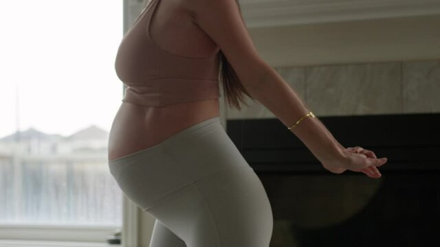 Athletic pregnant woman stetches for morning exercises - focus on 25 week pregnant belly