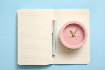 Alarm clock with notebook and pen on color background