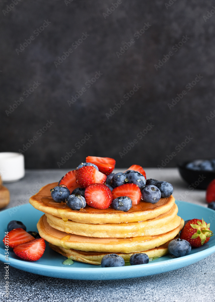 Canvas Prints Homemade pancakes in a blue plate with berries and syrup on a concrete background.