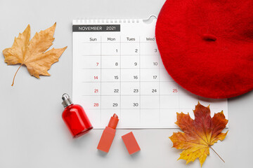 Calendar with female accessories and autumn leaves on light background