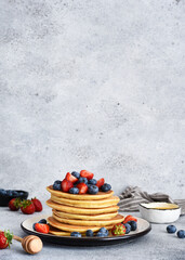 Stack of pancakes with berries and honey.on a concrete background.