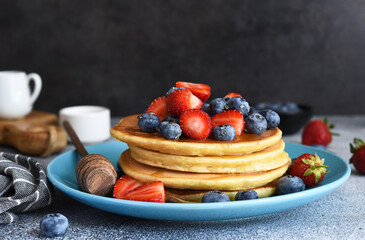 Homemade pancakes in a blue plate with berries and syrup on a concrete background.