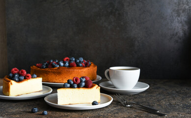 Cheesecake new york. Slice cheesecake with raspberries and blueberries, a cup of tea on a dark background. - obrazy, fototapety, plakaty