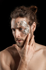Handsome young man with golden foil on face against black background
