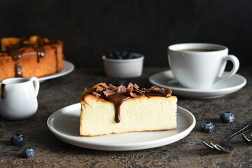 Cheesecake new york. Slice cheesecake with chocolate sauce and a cup of coffee on a dark concrete background.