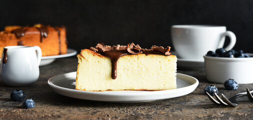 Cheesecake new york. Slice cheesecake with chocolate sauce and a cup of coffee on a dark concrete background.