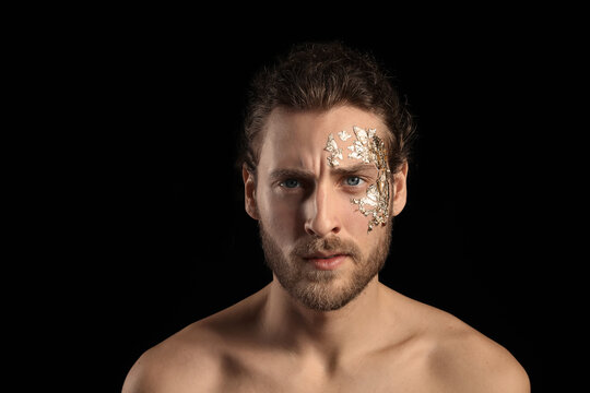 Handsome young man with golden foil on face against black background