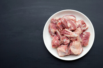 Raw pork ribs in white plate on dark background.