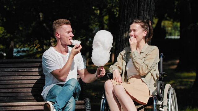 Young man and a woman in a wheelchair eating cotton candy in the park