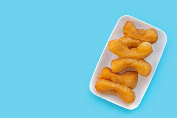 Deep-fried dough sticks or chinese bread sticks in white plate on blue background.