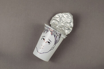 An empty cup of yogurt with face drawn on gray background. White plastic cup with foil lid....