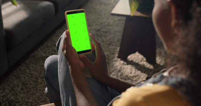 woman using smartphone watching green screen on mobile phone in vertical orientation person relaxing at home enjoying online entertainment
