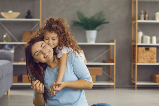 Hold me tight. Mother and child embracing each other and feeling happy. Mum and daughter sitting on floor in modern living room at home, hugging and smiling with eyes closed. Family and love concept