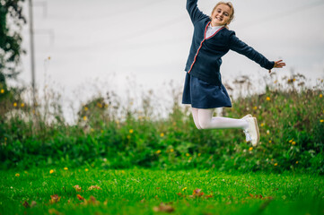 Full body portrait of happy positive schoolgirl  jumping up, wearing formal wear uniform outdoors....