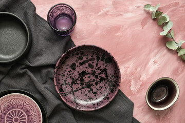 Stylish tableware and black napkin on color background