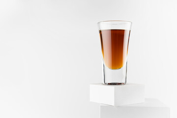 Bright brown brandy in glossy shot glass in sunlight with reflections on abstract white square podiums in soft light space, exquisite minimal style.