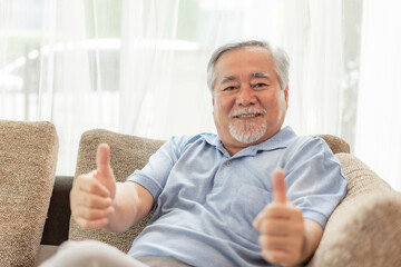 Portrait Asian senior man , old man giving a thumb up feel happy good health on couch living room interior background - lifestyle senior male at home concept