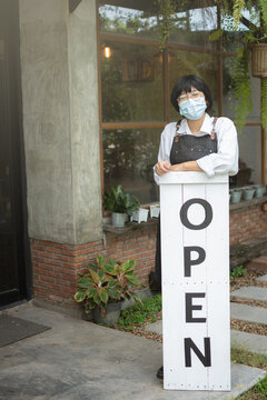 coffee shop owner holding wooden open sign in front of her shop