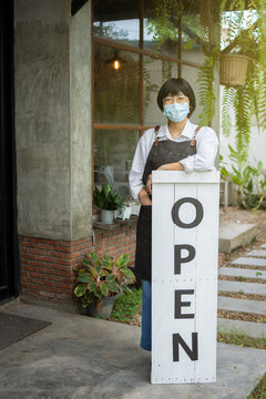 coffee shop owner holding wooden open sign in front of her shop