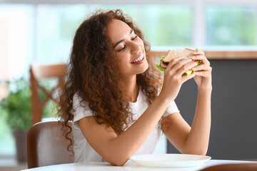Young African-American woman with tasty sandwich in kitchen
