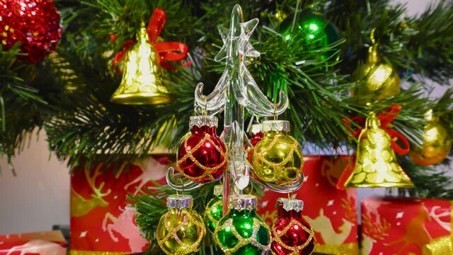 Little beautiful Christmas tree rotates on the background of a green Christmas tree and gifts