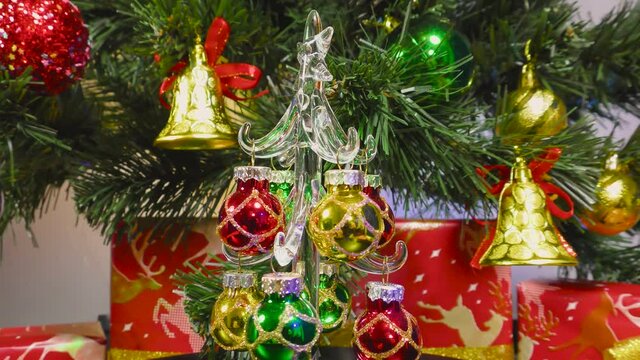 A small decorated Christmas tree rotates on the background of a green Christmas tree and gifts