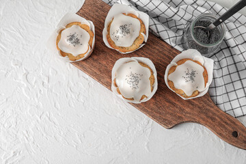 Wooden board with delicious glazed poppy seed muffins on light background