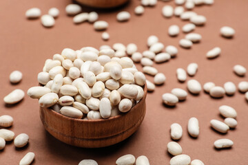 Bowl with raw beans on color background