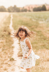 A little girl runs through a wheat field. The girl has fun and laughs with delight. Field with ripe ears of corn at sunset.