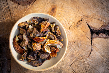 Dried boletus mushrooms in a ceramic bowl on a piece of natural wood. Organic freshly sliced forest harvest. Selective focus on food, blurred background.