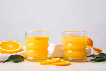 Glasses of tasty orange juice on light background