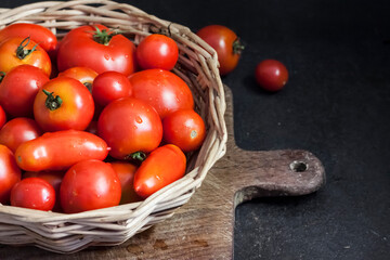 Fresh red tomatoes in whicker basket on black background