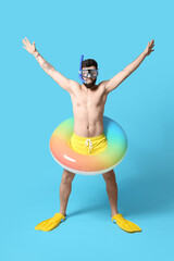 Funny young man with inflatable ring, paddles and snorkeling mask on color background
