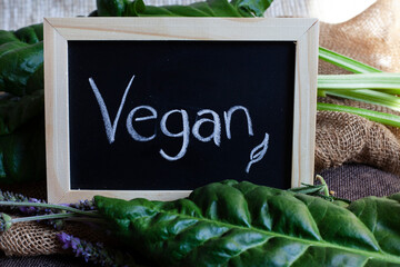 chalkboard with fresh green leafy vegetables with the word vegan written down