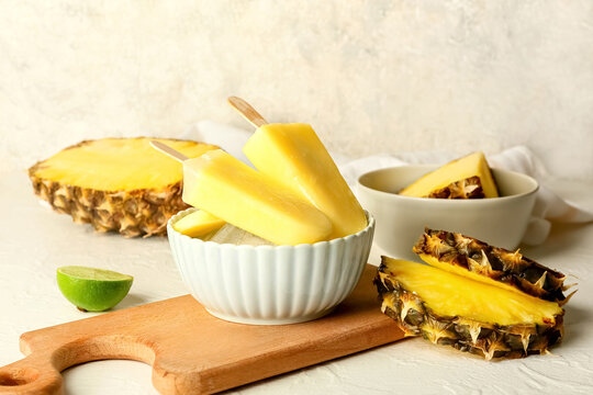 Board with tasty pineapple popsicles on light background