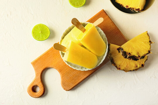 Board with tasty pineapple popsicles on light background