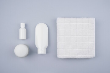 Plastic white tubes for cream or lotion on the background of a white towel. Top view of bathing set on grey background. Skincare natural cosmetic