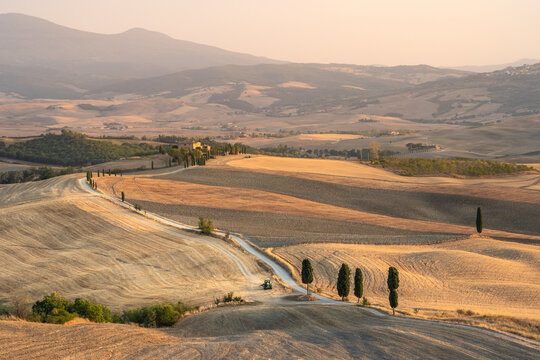 Beautiful tuscanian landscape at sunset, with dirt track curving between harvested wheat fields and cypress trees