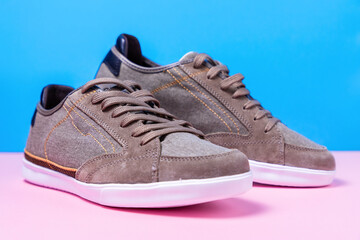 Pair of man's new sneakers made of grey canvas laid out on a pink-blue background. Close up