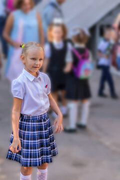 portrait, a child in the schoolyard, the beginning of the school year, a little girl, a first grader, 7 years old, a blonde in a school uniform, in a white blouse and a plaid skirt