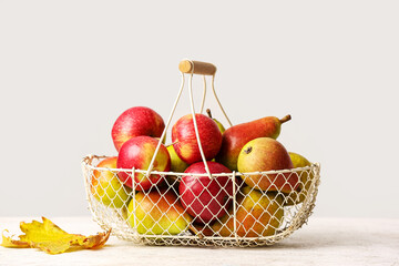 Basket with ripe pears and apples on light background