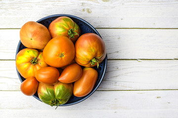 Red tomatoes in a dark plate on a light wooden background. Harvesting concept. Flat lay.