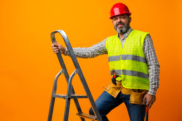 Handyman in uniform standing with ladder against orange background