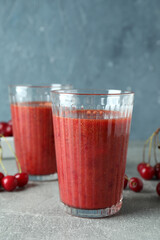 Glasses of cherry smoothie and ingredients on gray textured table