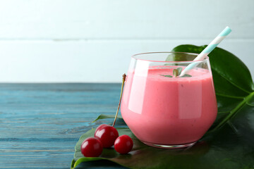 Glass of cherry smoothie and ingredients on palm leaf, on wooden table